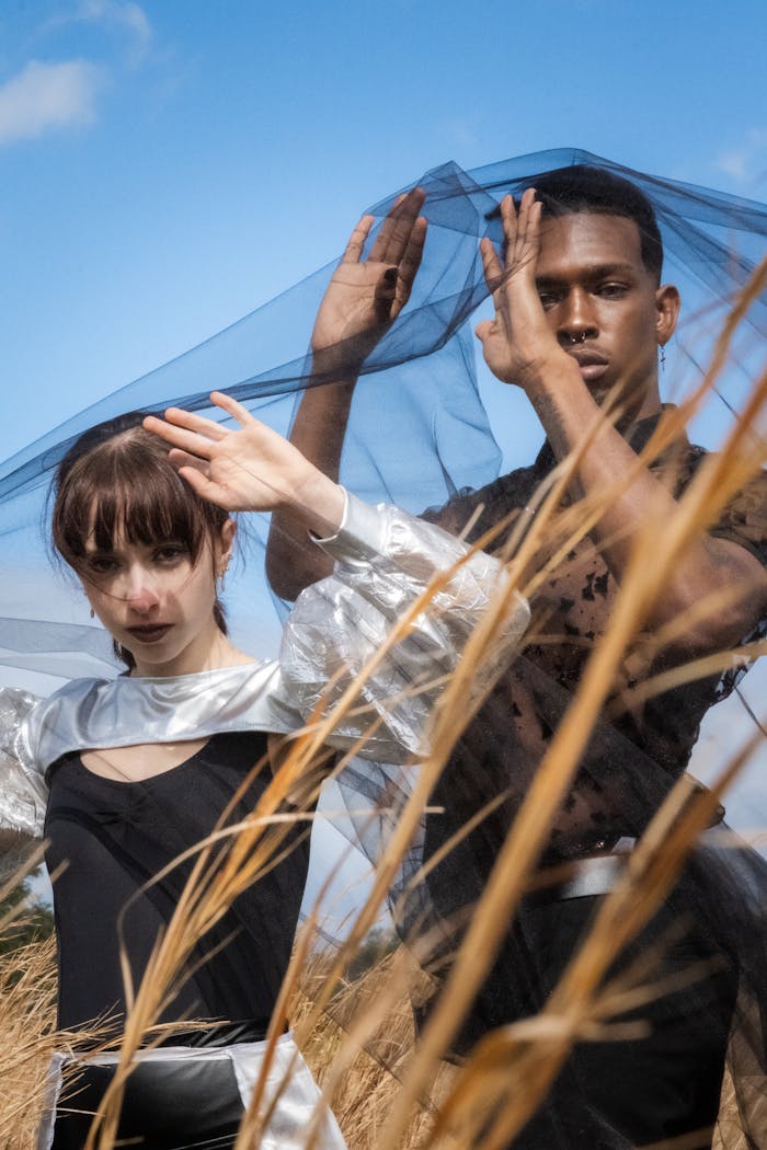 A stylish fashion shoot featuring two models draped in black veil outdoors.